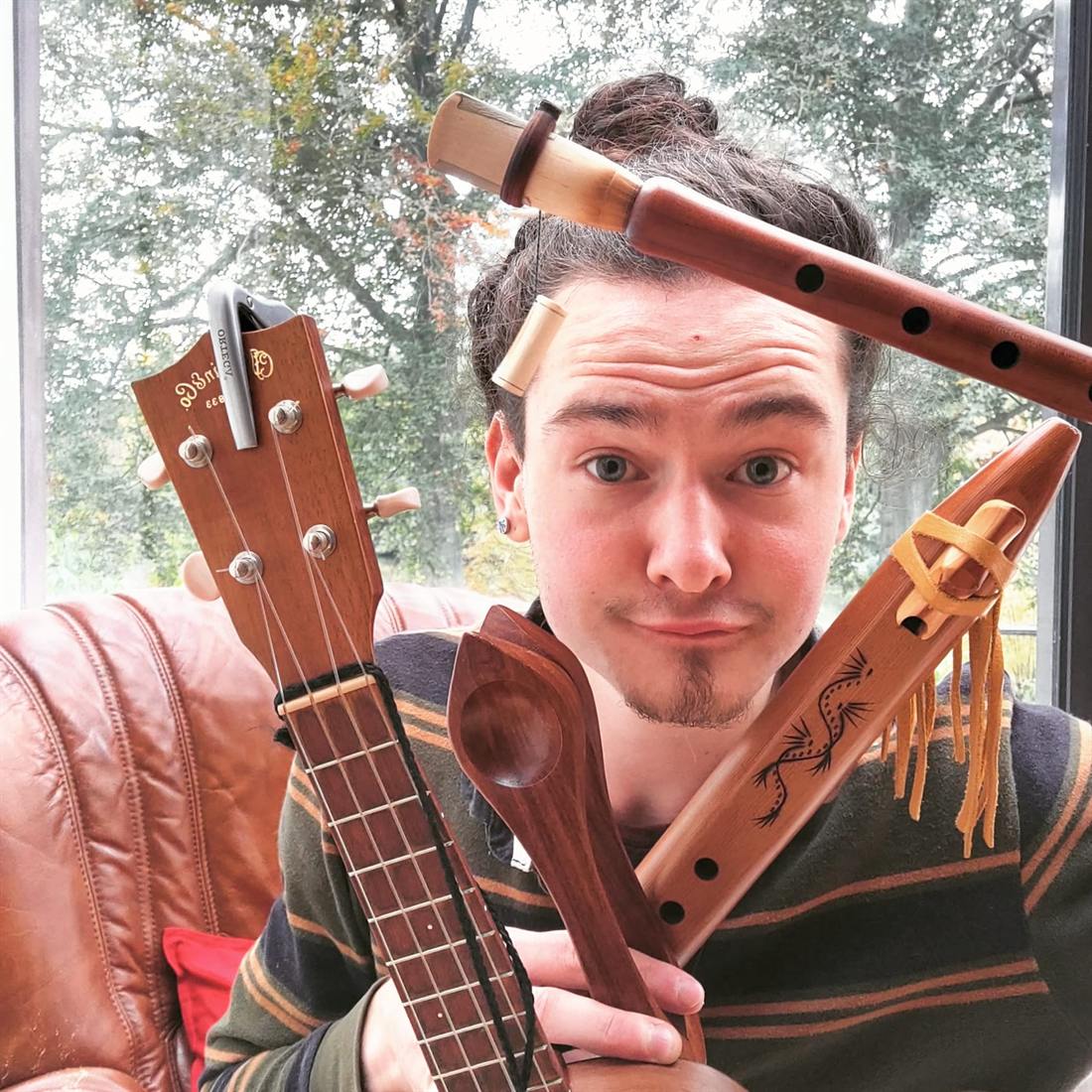 Thomas holding a ukulele, two flutes and a carved wooden spoon